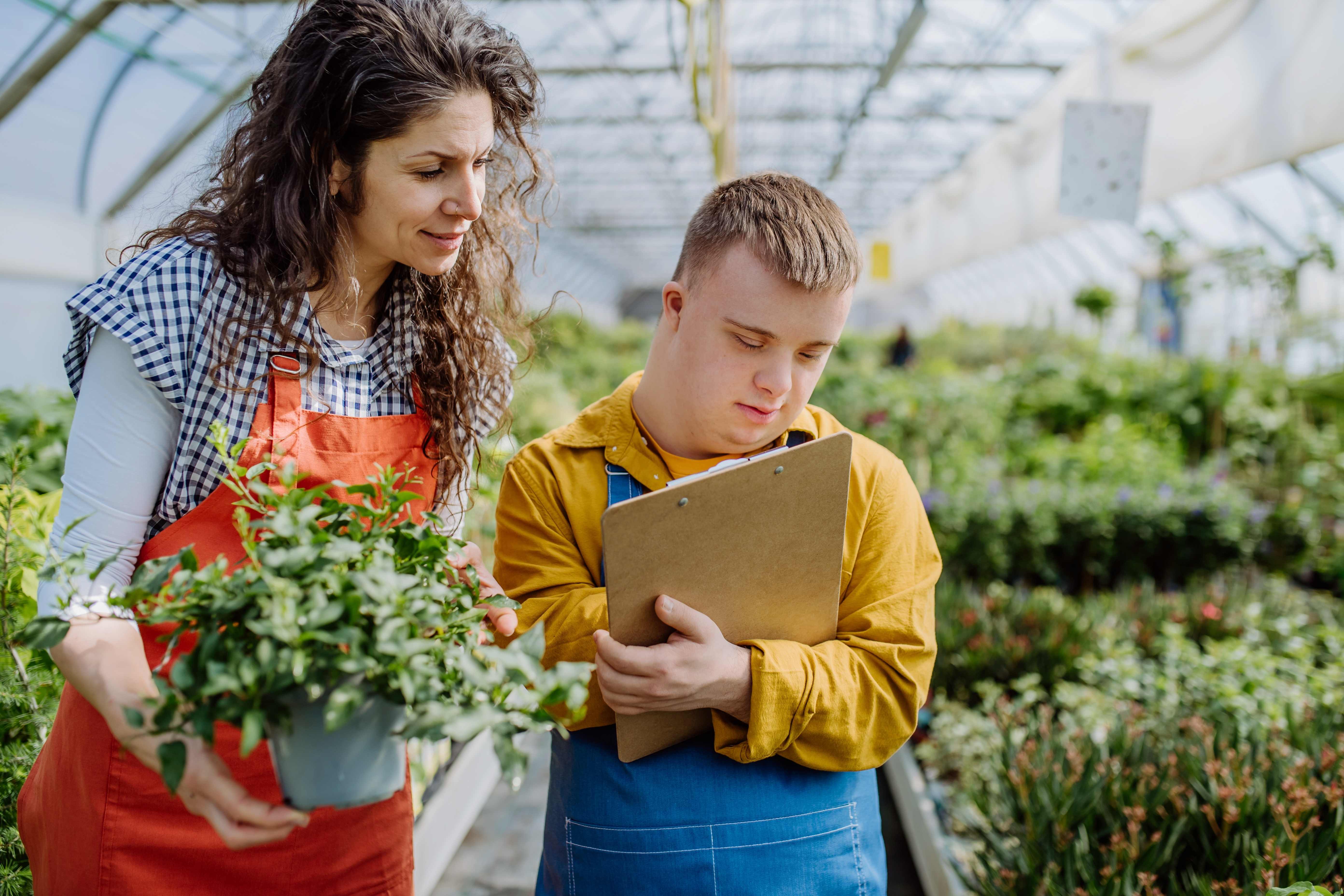 Staff member teaching vocational skills to young man with Down syndrome in greenhouse